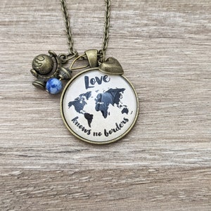 May include: A necklace with a round pendant featuring a world map and the text "Love knows no borders". The pendant is attached to a brown chain with a small globe charm and a blue bead.
