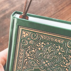 May include: A green hardcover journal with a gold embossed design and a brown leather bookmark. The title "The Secret Garden" is visible on the cover.