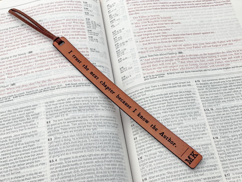 May include: A brown leather bookmark with the text "I trust the next chapter because I know the Author." and the initials "MK" in the bottom right corner.