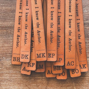 May include: A set of brown leather bookmarks with the text "because I know the Author." printed on each one. The bookmarks are stacked on top of each other and have different initials on the bottom.