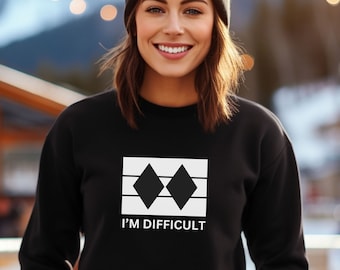May include: Black sweatshirt with a white graphic of two black diamonds in a rectangle with the text "I'M DIFFICULT" underneath. The model is wearing a black beanie.