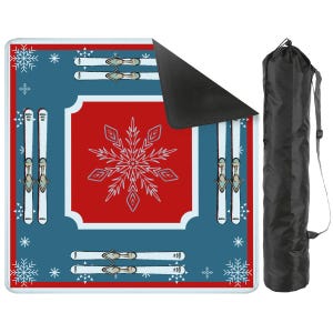 May include: A square outdoor blanket featuring a red center with a large white snowflake, surrounded by a blue border with white snowflake patterns and pairs of white skis. The blanket has a black underside and includes a black carrying bag.