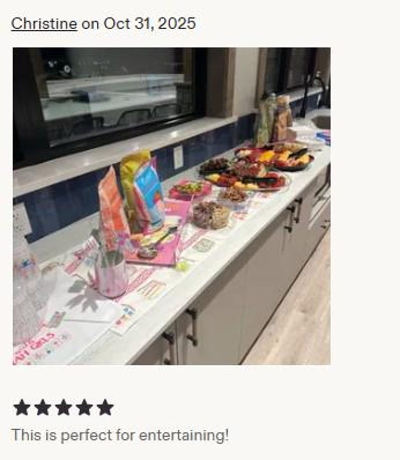 May include: A kitchen counter covered with a white runner featuring pink and blue graphic illustrations of cakes and the text "AH GIRLS". The runner is topped with various snack bags, bowls of food, and a pink patterned cup with metal utensils.