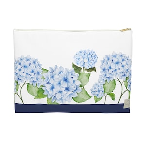 Può includere: Pochette con cerniera bianca con un design ad acquerello di fiori di ortensia blu e foglie verdi. Una striscia blu navy accentua il fondo. La pochette ha una cerniera color oro.