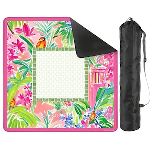 May include: A colorful outdoor blanket with a vibrant floral and bird design in pink, green, and orange. The blanket has a black underside and a matching black carrying bag with a shoulder strap. The blanket features a decorative border and a central patterned area.