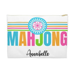 Può includere: Pochette bianca con cerniera con la scritta "MAHJONG" in lettere colorate. Sopra il testo c'è un motivo a strisce orizzontali in oro, arancione, rosa, verde e blu. Un motivo floreale è centrato sopra la parola "MAHJONG". Il nome "Annabelle" è scritto in corsivo sotto.