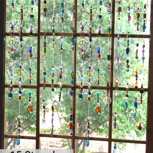 May include: Fifteen strands of colorful beaded curtains hang in a window. The beads are various shapes and sizes, and the colors are bright and vibrant. The curtains are made of clear string and are hung from a wooden frame.