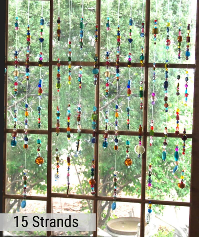 May include: Fifteen strands of colorful beaded curtains hang in a window. The beads are various shapes and sizes, and the colors are bright and vibrant. The curtains are made of clear string and are hung from a wooden frame.