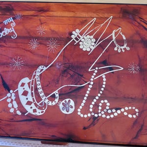 May include: A vintage jewelry box with a red-brown marbled finish. The lid features a silver-colored design of a hand holding a necklace and bracelets with the words "for my jewelry" written in cursive.