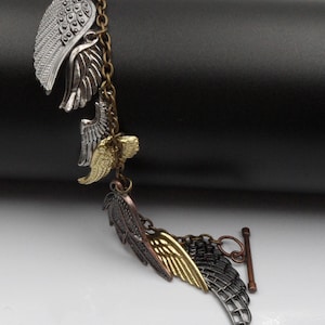 May include: A silver and gold tone bracelet with multiple angel wing charms. The bracelet has a toggle clasp.