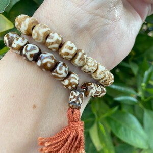 May include: Two brown and white beaded bracelets with a brown tassel. The bracelets are worn on a person's wrist.