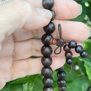May include: A dark brown wooden beaded necklace with a brown cord tie. The beads are round and smooth.