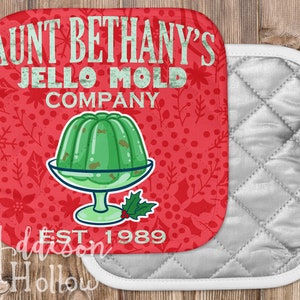 May include: Aunt Bethany's Jello Mold Company pot holder with a green jello mold graphic on a red background. The pot holder has a silver quilted backing and white trim. The text "EST. 1989" is also visible.