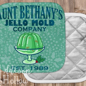May include: Square pot holder with a teal background featuring the text "Aunt Bethany's Jello Mold Company" and a green jello mold graphic. The pot holder has a white border and a quilted silver backing. The text "EST. 1989" is also visible.