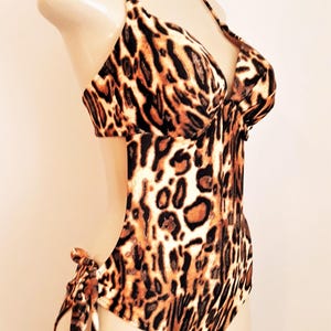 May include: A brown and black leopard print swimsuit with a halter top and a cutout on the side. The swimsuit has a tie at the side.