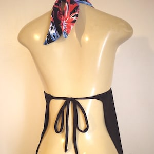 May include: Black halter top with a floral patterned neck tie. The tie features red, blue, and purple flowers on a black background. The top is tied at the back with a bow.