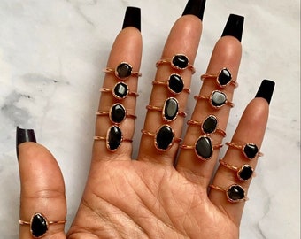 Puede incluir: Un maniquí de mano con múltiples anillos de oro con piedras preciosas ovaladas negras. Los anillos están apilados en cada dedo.