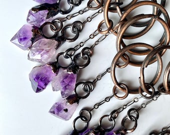 May include: A set of amethyst crystal charms with copper accents hanging from a chain on a copper ring. The charms are attached to the chain with small copper rings.