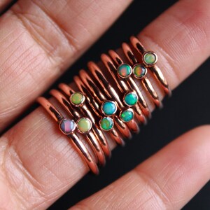 May include: A stack of delicate copper rings with small opal gemstones in various shades of green, blue, and pink.