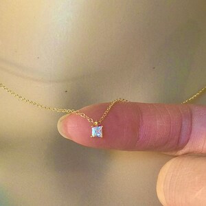 Puede incluir: Un delicado collar de cadena de oro con un pequeño colgante de piedra preciosa transparente de forma cuadrada.