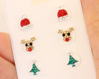 May include: A white card with six pairs of Christmas-themed earrings. The earrings are made of rhinestones and feature a Santa hat, a reindeer, and a Christmas tree.