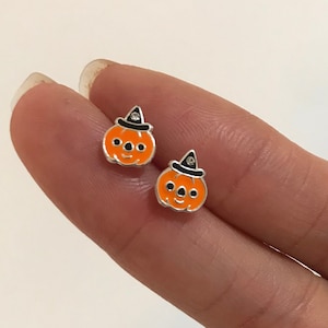 May include: A pair of silver pumpkin earrings with black witch hats and orange faces. The earrings are small and dainty.