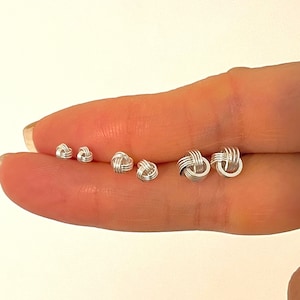 May include: A set of five silver knot earrings of varying sizes, displayed on a finger.