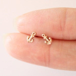 May include: A pair of gold anchor stud earrings. The earrings are small and delicate, and they are perfect for everyday wear.