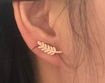May include: A gold leaf-shaped earring with a delicate design. The earring is worn in the upper lobe of the ear.