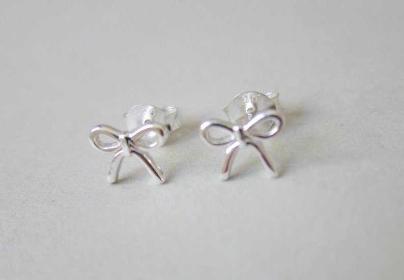 May include: A pair of silver bow-shaped stud earrings.