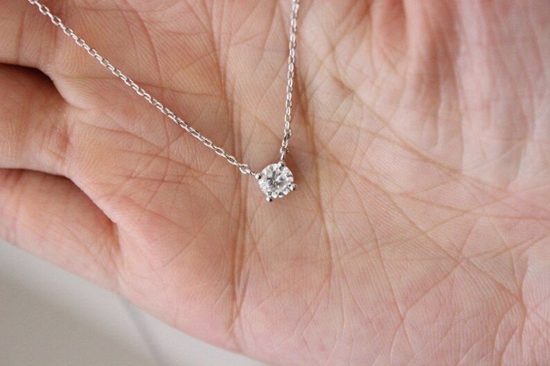 May include: A delicate silver chain necklace with a single, round, clear diamond pendant.