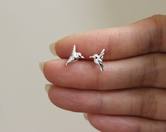 May include: A pair of silver hummingbird earrings. The earrings are small and delicate, and they feature a realistic hummingbird design.