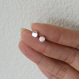 May include: A pair of small, round, silver stud earrings. The earrings have a hammered texture.