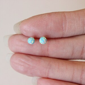 May include: A pair of small, round, light blue opal stud earrings. The earrings are set in silver.