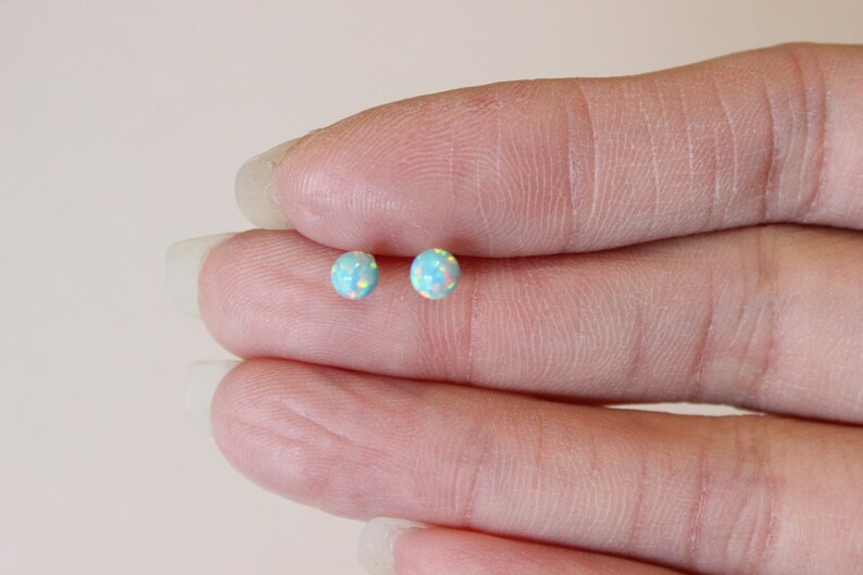 May include: A pair of small, round, light blue opal stud earrings. The earrings are set in silver.