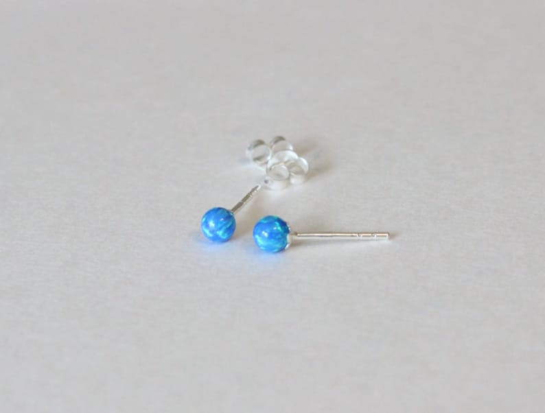 May include: A pair of silver stud earrings with blue opal stones.