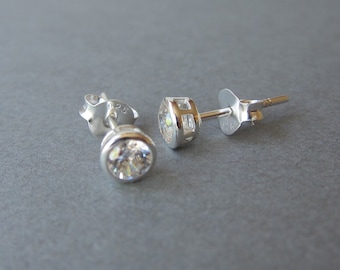 May include: A pair of silver stud earrings with clear round cubic zirconia stones. The earrings have a post and butterfly back.