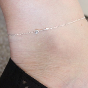 May include: A silver ankle bracelet with a small arrow charm.