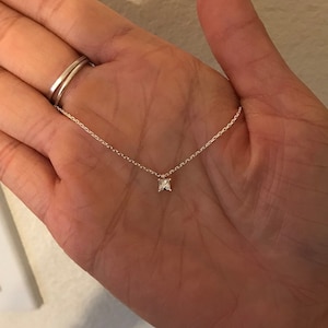 May include: Delicate silver necklace featuring a small, square-cut gemstone pendant. The pendant is centered on a fine chain, creating a minimalist and elegant design. The necklace is shown against a neutral background.