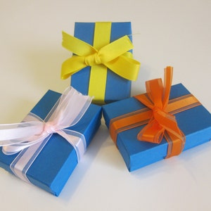 May include: Three blue gift boxes with different colored ribbon bows. The boxes are tied with yellow, pink, and orange ribbon.