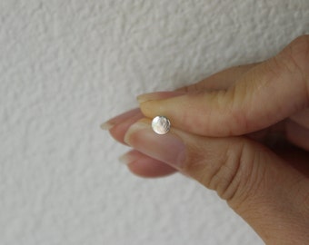 May include: A small, round, silver earring with a textured surface.