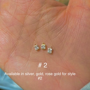May include: Three small, square-cut, clear gemstone pendants with gold-colored settings. The pendants are displayed on a light-toned background. The text "#2" and "Available in silver, gold, rose gold for style #2" are also visible.