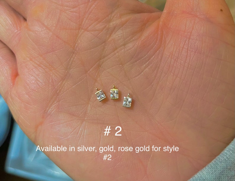 May include: Three small, square-cut, clear gemstone pendants with gold-colored settings. The pendants are displayed on a light-toned background. The text "#2" and "Available in silver, gold, rose gold for style #2" are also visible.