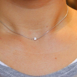 May include: A delicate silver chain necklace with a small, round, clear gemstone pendant.