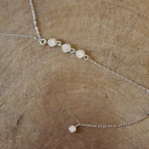 May include: A silver chain necklace with a single dangling crystal and four crystals in a row.