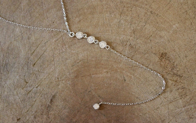 May include: A silver chain necklace with a single dangling crystal and four crystals in a row.