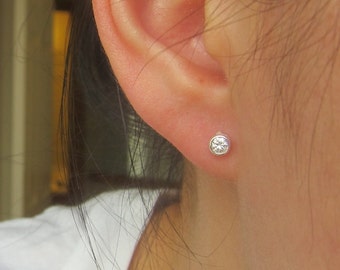 May include: A close-up of a person's ear with a small, round, clear diamond stud earring.
