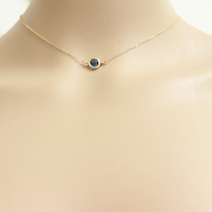 May include: A delicate gold chain necklace with a small, round blue gemstone pendant.