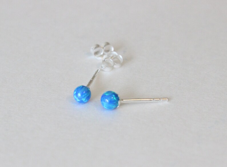 May include: A pair of silver stud earrings with blue opal stones.
