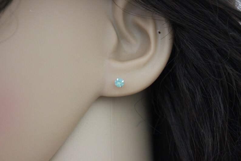 May include: A pair of small, round, light blue stud earrings. The earrings are set in silver.